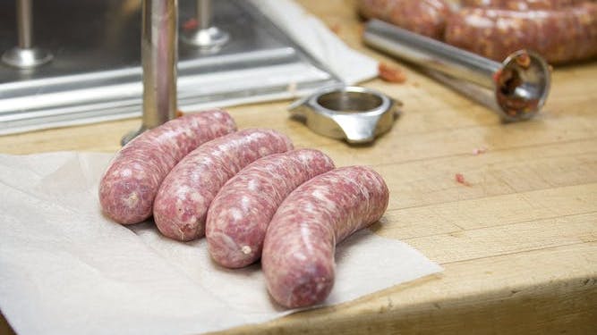 Four fresh sausages displayed on a butcher table with sausage making equipment in the background.