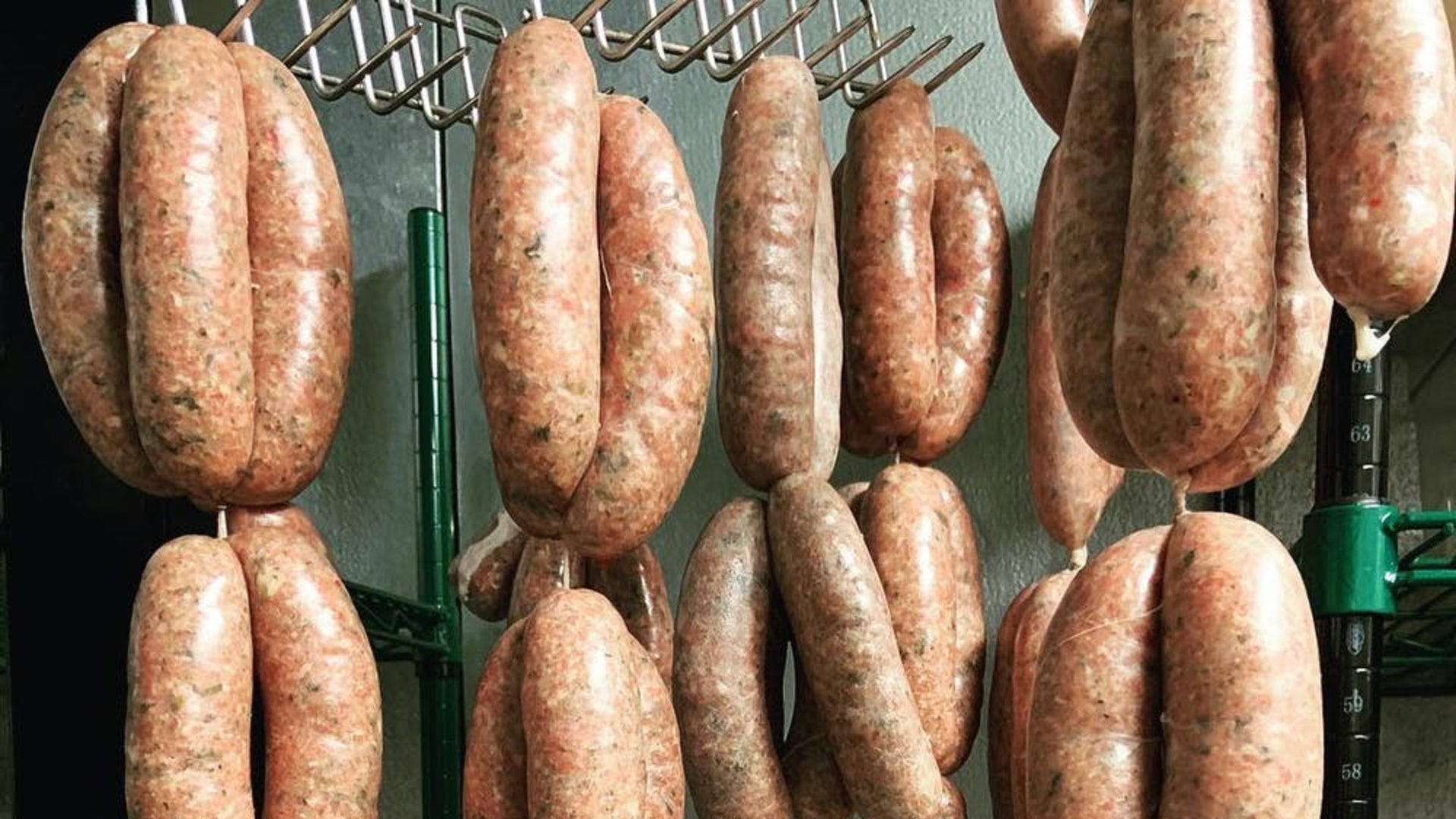 Several sets of sausage links hanging in a smoker to show the equipment needed to smoke sausages when they're hanging.