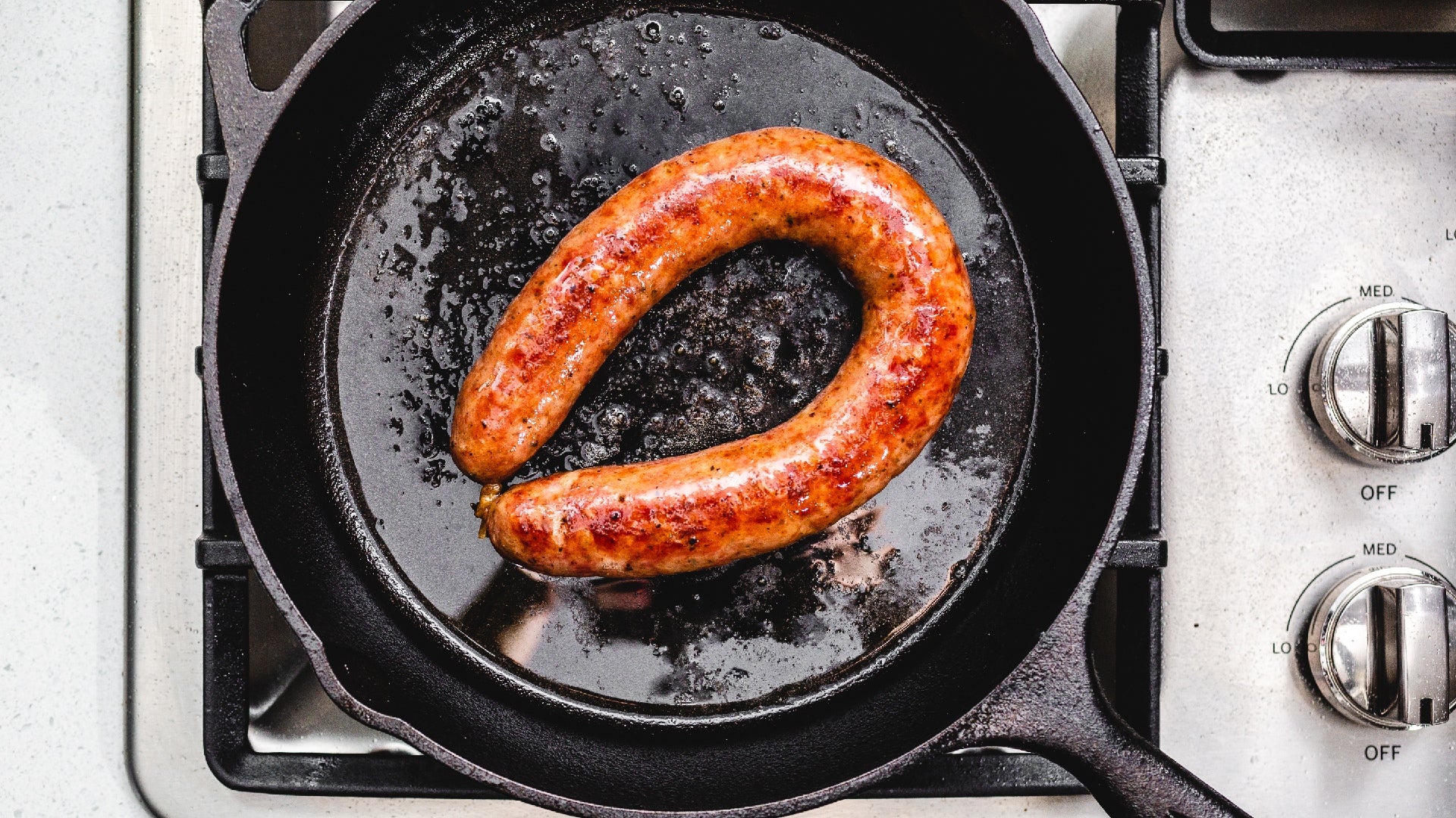 Kielbasa sausage cooking in cast iron skillet and shot from above.