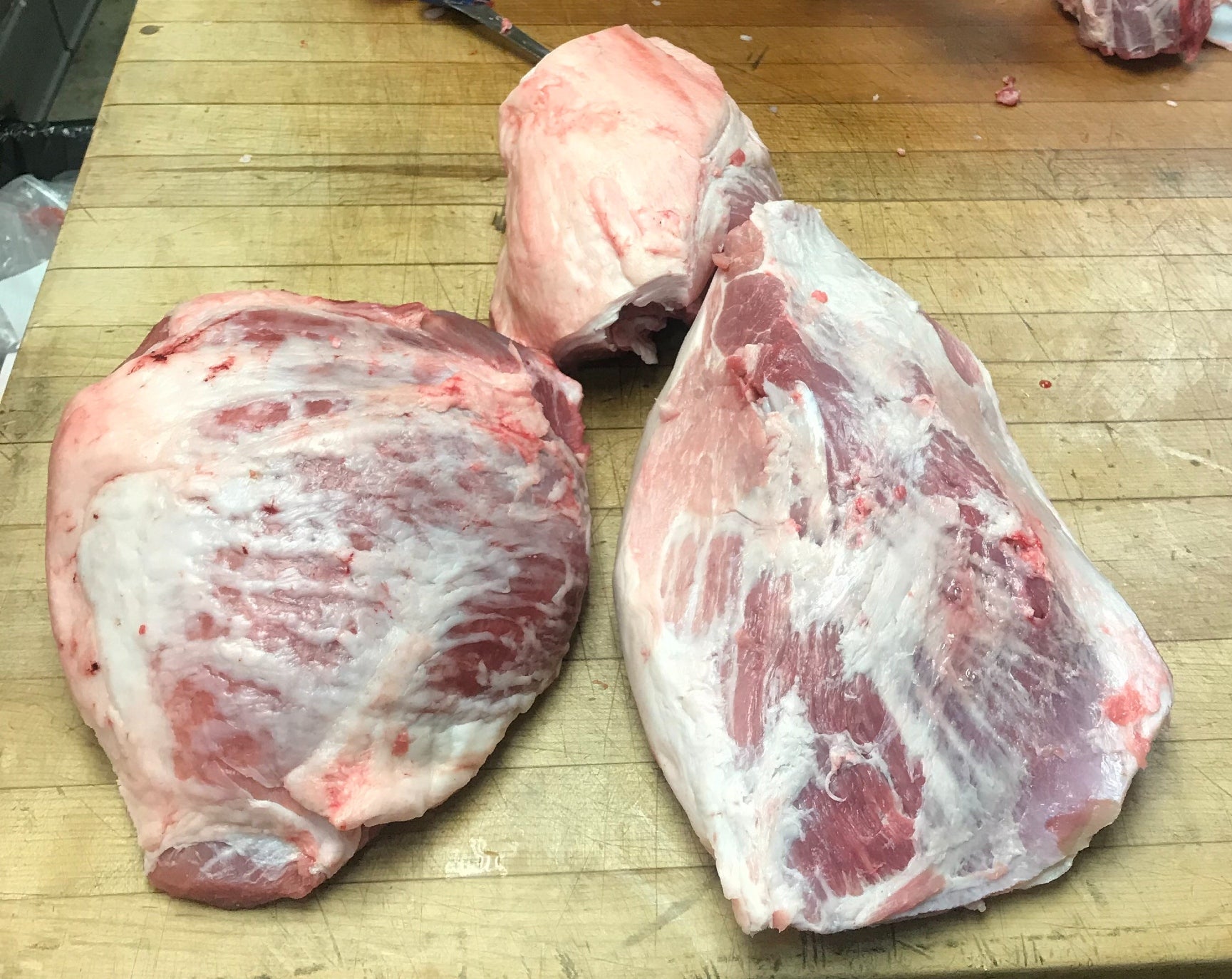 A picture showing the three main muscle cuts from the hind leg of a pig on a butcher table.
