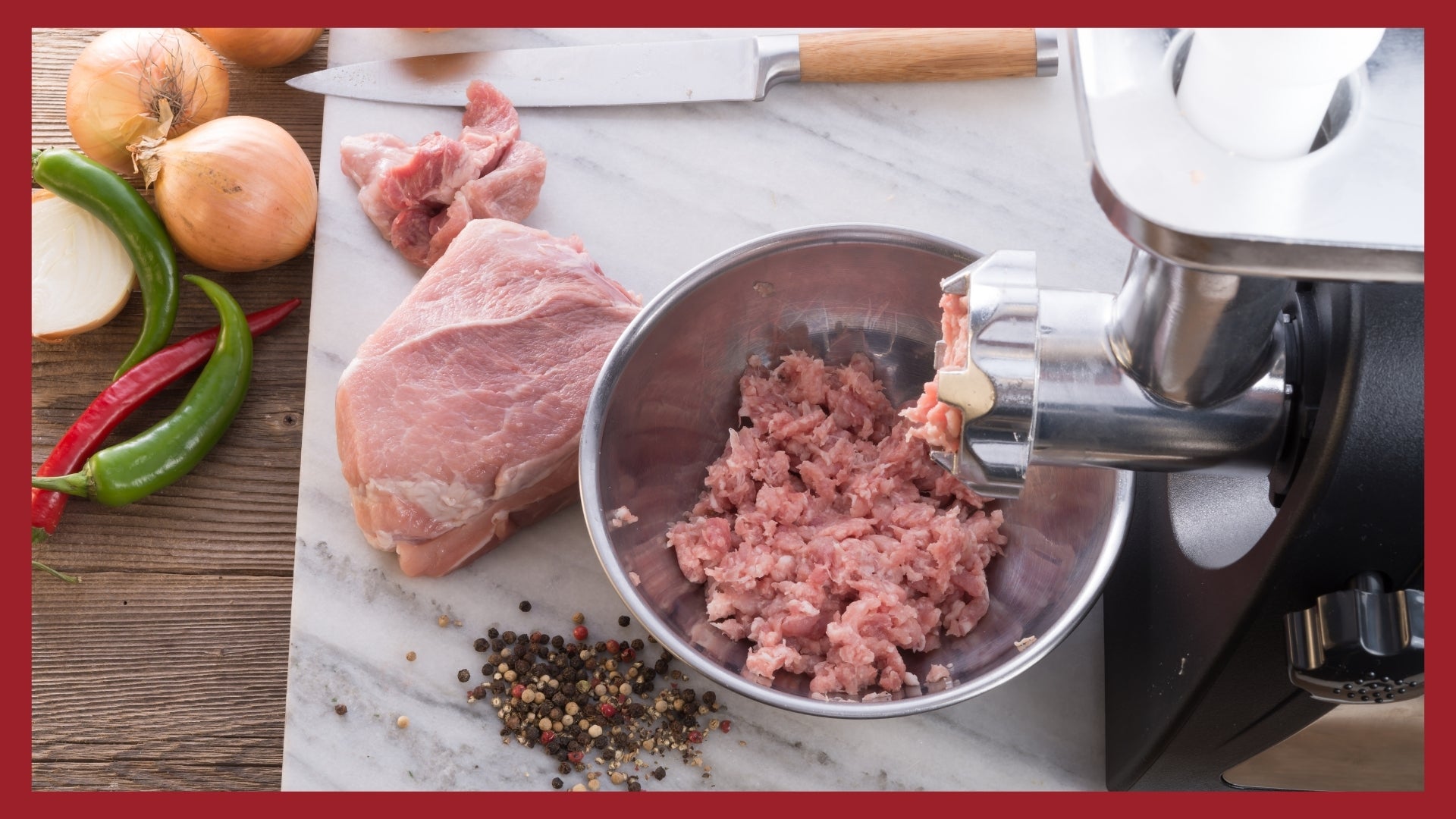 A picture showing the end of a meat grinder with ground pork coming out of it and falling into a bowl. Whole pork muscle cuts, veggies and spices are on a cutting board next to the bowl holding the ground pork.