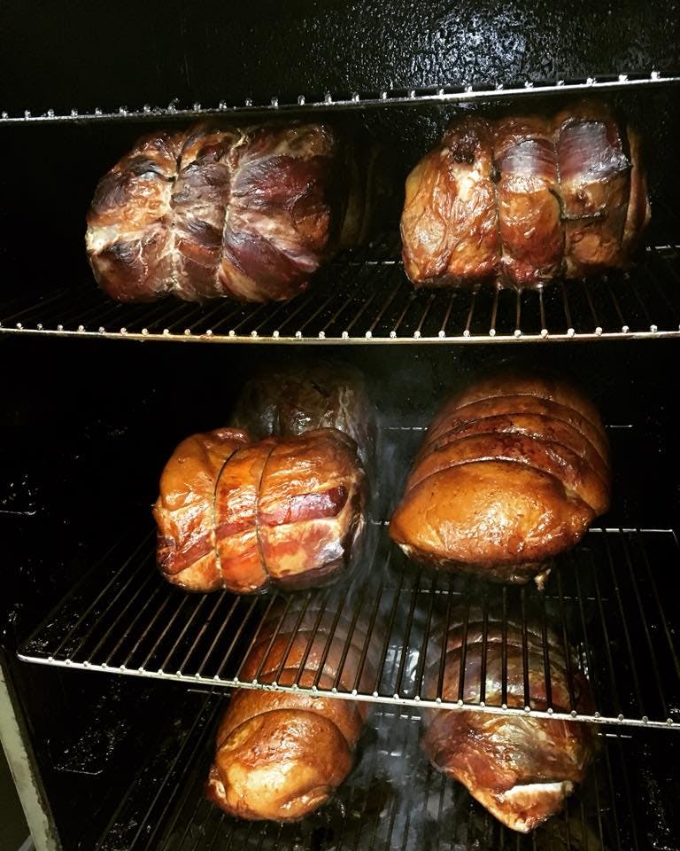 A picture showing three racks in a smoker holding hams as the go through the smoking process.