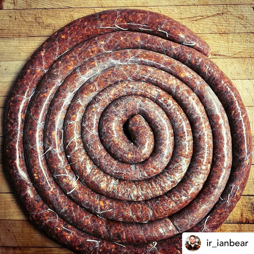 Several feet of specialty sausage rolled up on a butcher table and pictured from above.