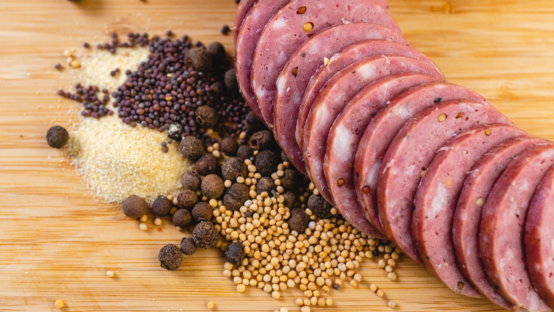 A close up picture of slices of summer sausage on a cutting board with herbs and spices next to them.