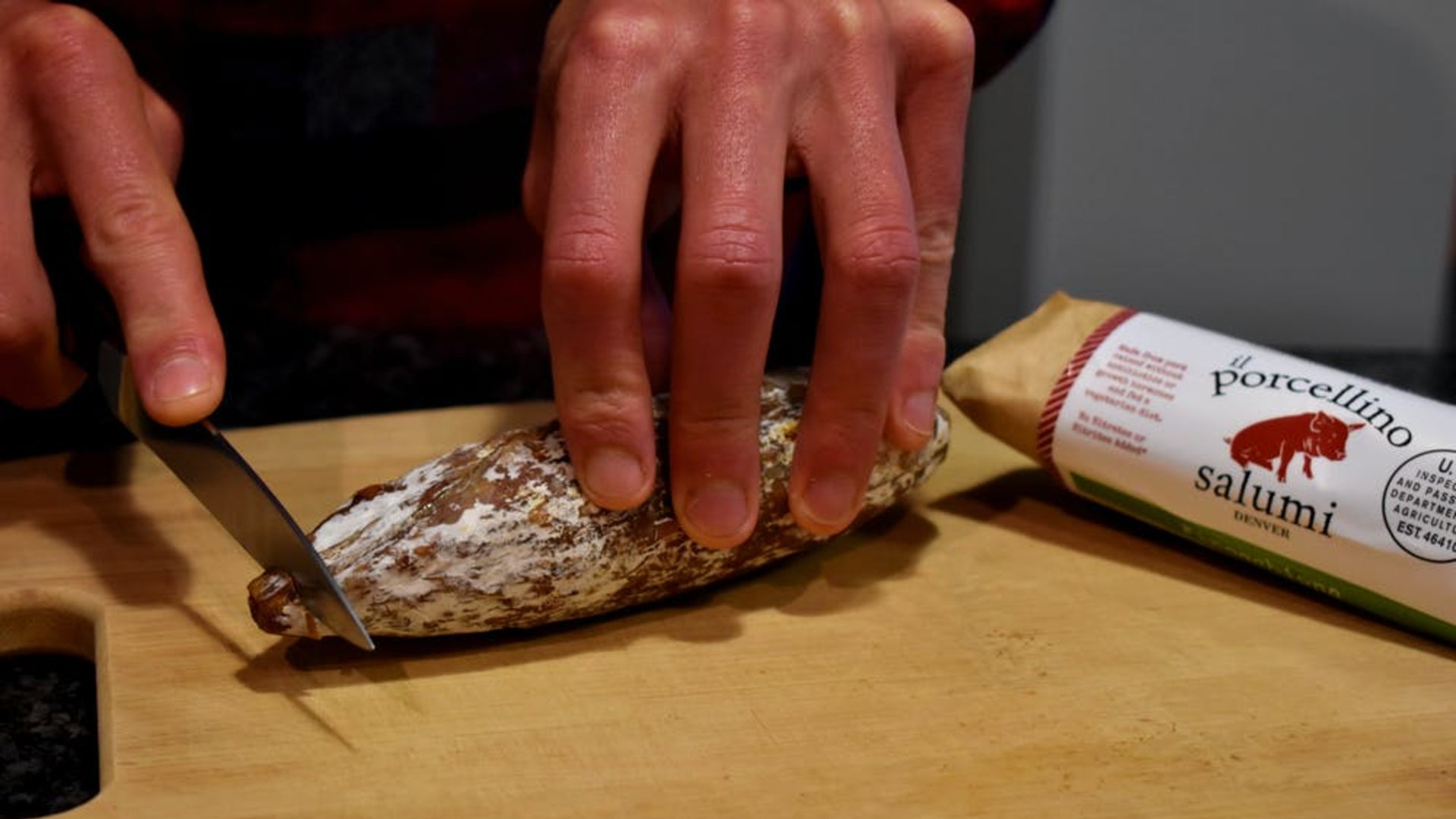 A picture of someone cutting a salami on a cutting board to show that it's okay to touch the protective salami mold.