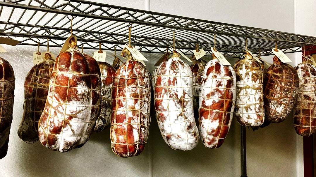 il porcellino salumi's large format salami hanging in the drying room to display the different colors of protective mold that form.