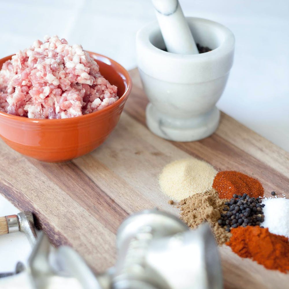 A picture with ground meat in a bowl, next to herbs and spices on a cutting board.