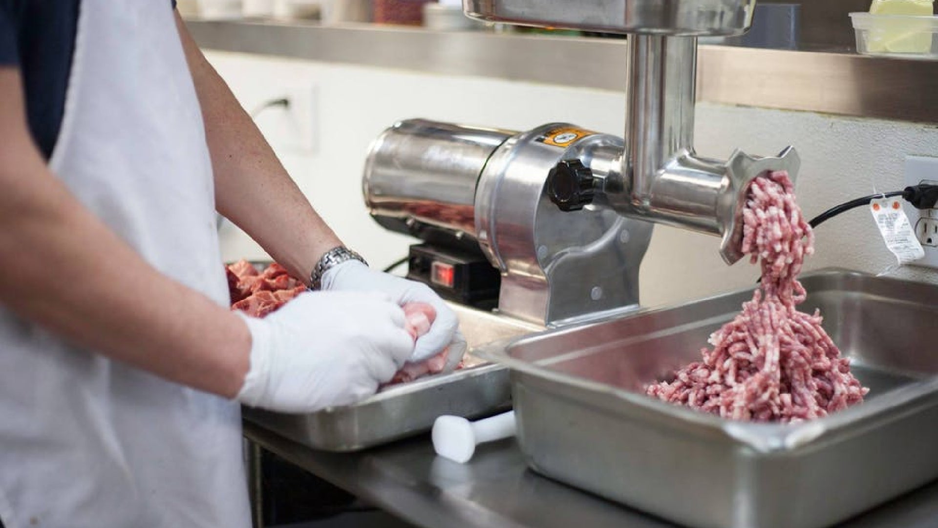 A picture showing someone grinding pork as the freshly ground pork falls into a pile in a tub.