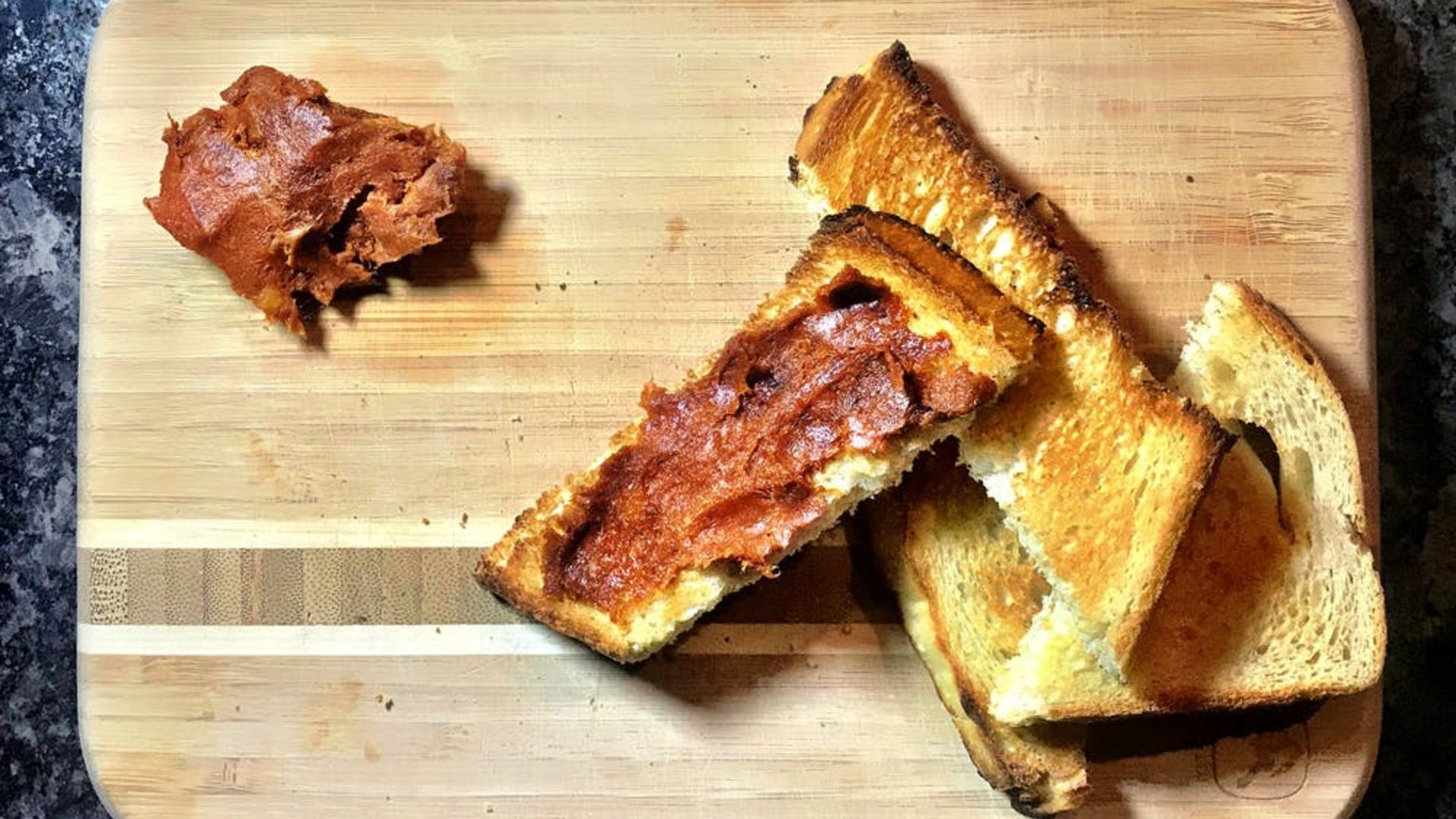 four pieces of crispy toasted bread on a cutting board with 'nduja spread on one piece.