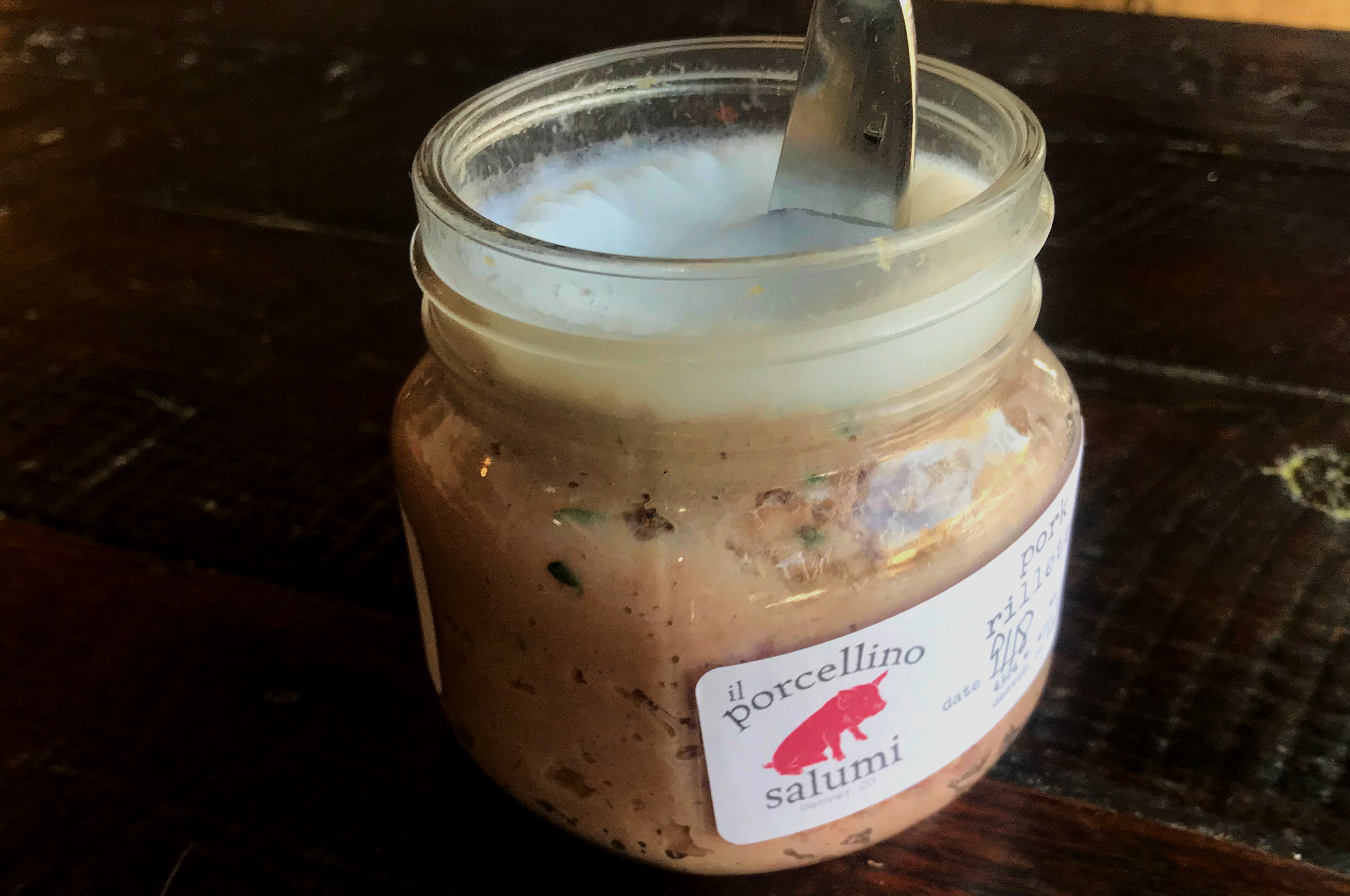 A picture of jarred pork rillette on a dark table with a knife in it. 