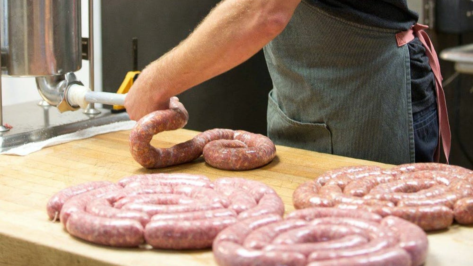 Someone using a sausage stuffing machine to make fresh sausage. Plus several recently stuffed sausage casings rolled up on a butcher table.