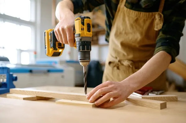 Carpenter working with drill leaning over table at carpentry workshop