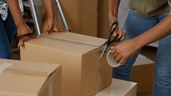 People wrapping up cardboard boxes with sticky tape roller