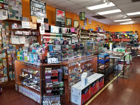 "Interior view of a smoke shop showcasing a wide variety of products. Shelves are lined with colorful glass pipes, bongs, vape devices, and smoking accessories. The shop features well-lit displays, a counter with additional merchandise, and a welcoming atmosphere for customers exploring the diverse selection of smoking-related items."