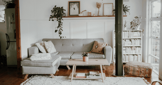 Salón estilo nórdico con sofá esquinero gris, mesas de madera y plantas