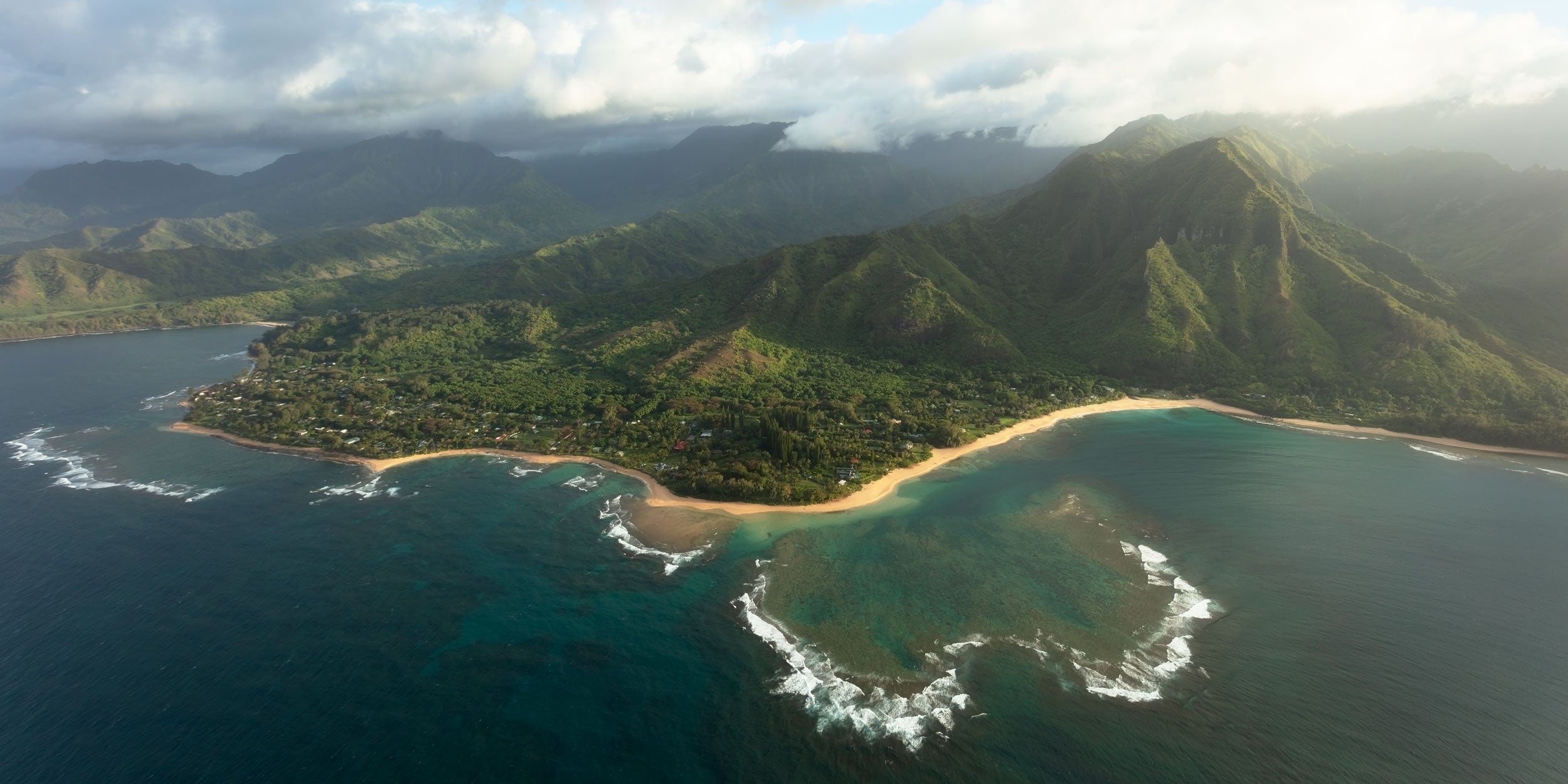 An aerial photograph taken on a Kauai helicopter tour of the Napali coast on Kauai, Hawaii, of the Tunnel Beach, Ke'e Beach and Haena area where the Kalalau trail hike backpacking adventure leaves from at sunset.