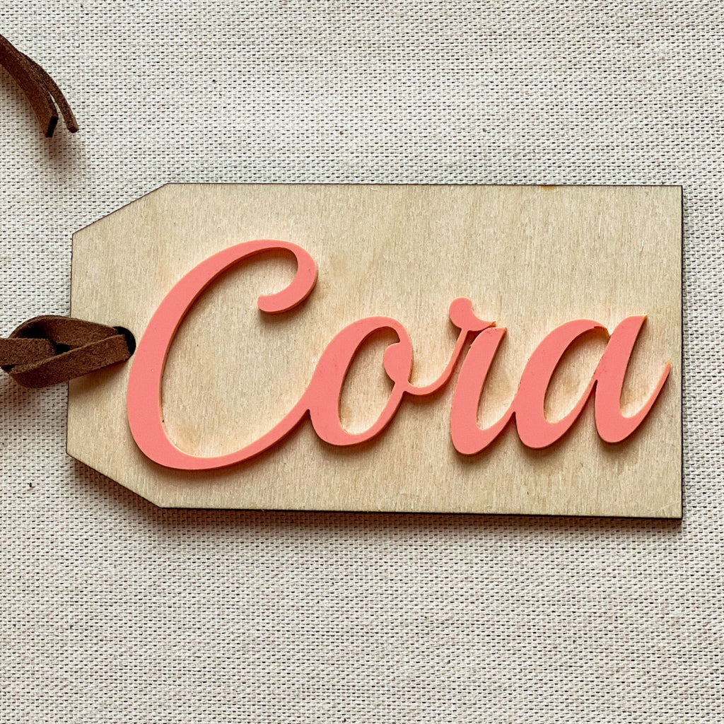 Customized name tag in Coral with the name Cora on a beige surface. 