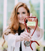An attractive white female doctor holding a red stethsascope in the shape of a heart.