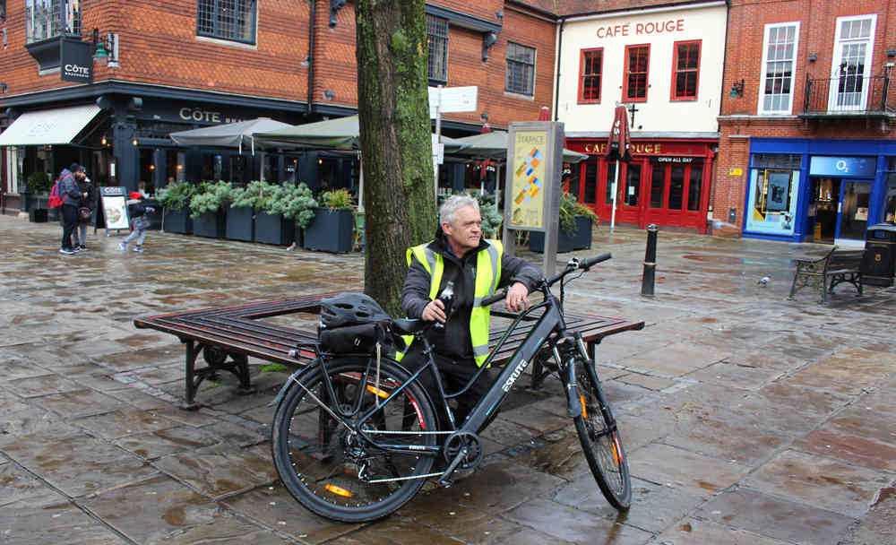 A man on an electric bicycle parked next to a seat under a tree