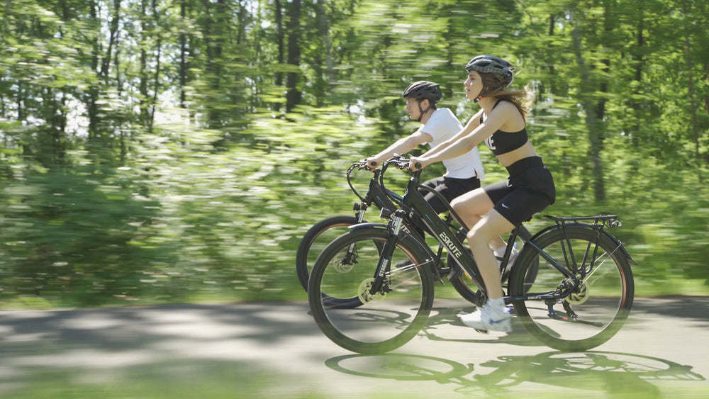 a man and a woman with MTB helmets are riding e-bikes on the shadowy path