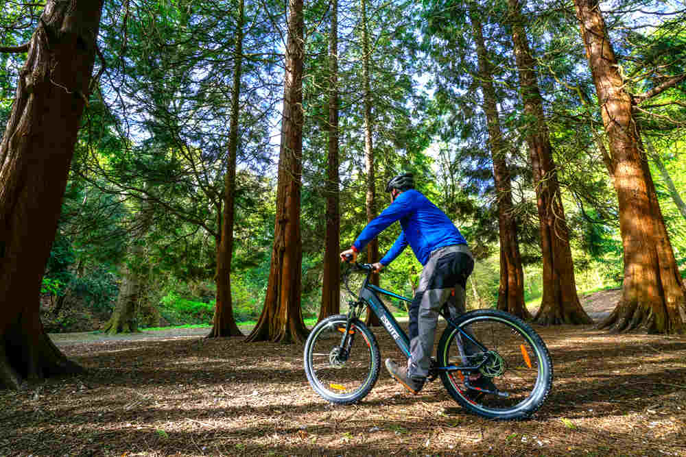 a man wearing waterproof trousers ride his e-bike in the mountainous forest