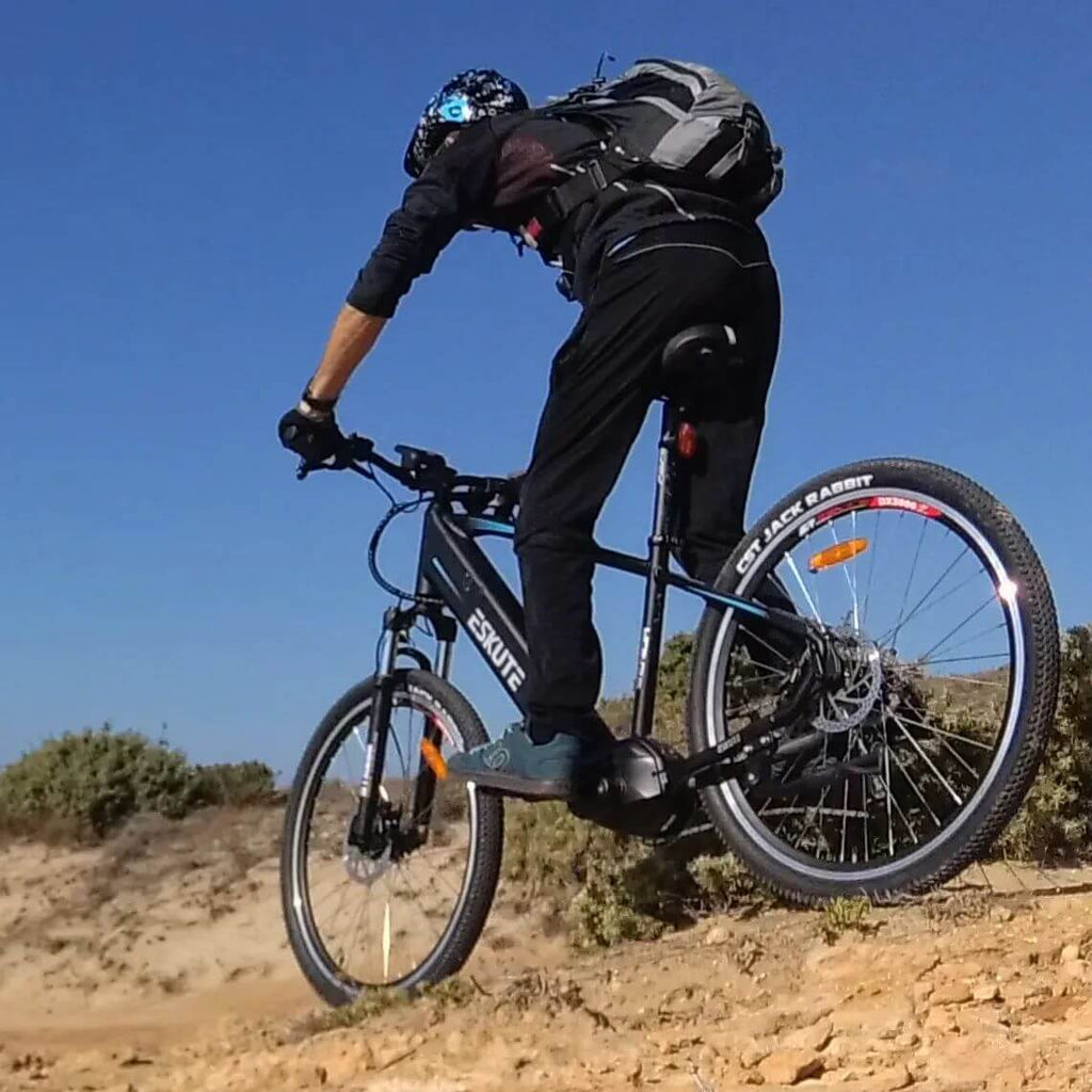 a man with a helmet and backpack is pedalling uphill by ESKUTE mountain bike
