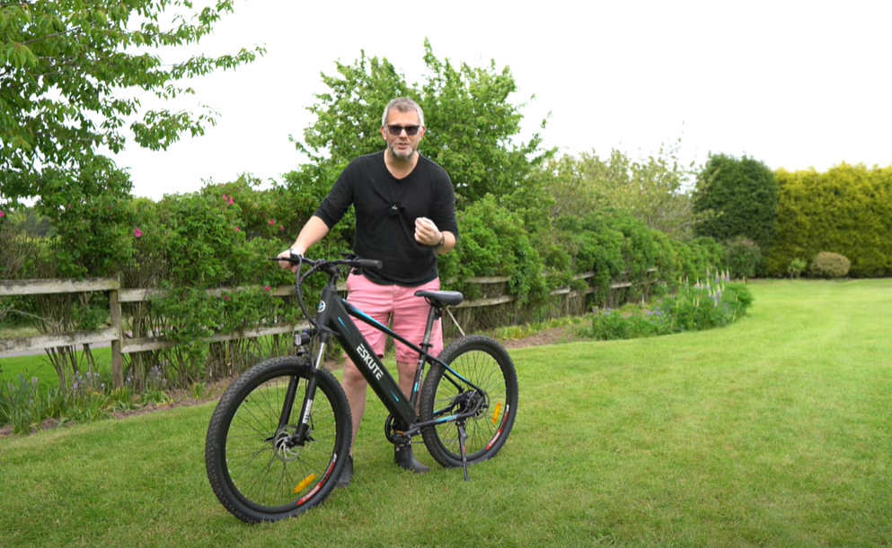 a man with glasses is introducing his e-bike on the grasslands before mountain biking