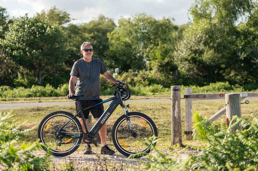 a man with glasses is standing with The Most Comfortable E-Bike-Netuno E-Mountain Bike