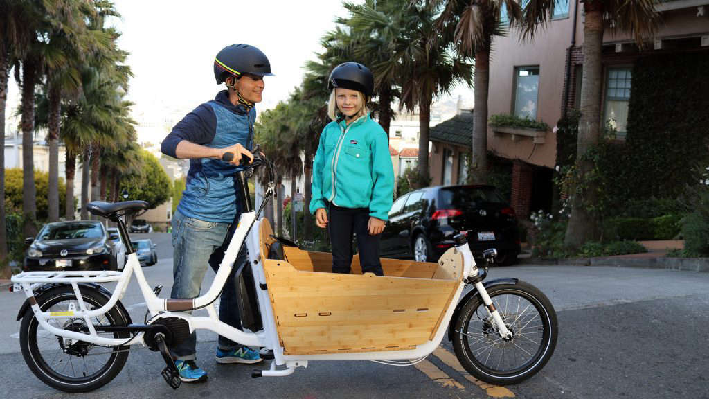 a mom stands by the electric cargo bike and her daughter stands in the coach