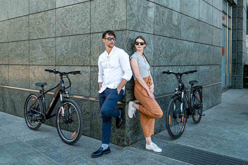 a man and a woman are leaning against the wall and leaving their electric bikes besides