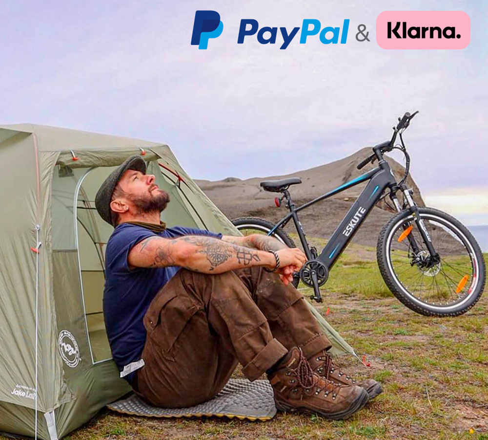 a man sits on the ground and leans on the tent with his ebike