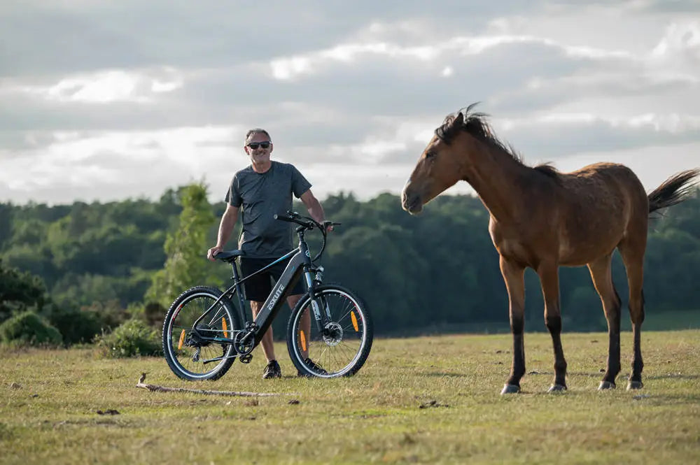 man stand with his E-Mountain Bike besides a horse