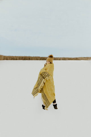 Jessica standinding on a frozen lake with Turmeric Kos throw blanket wrapped around her.