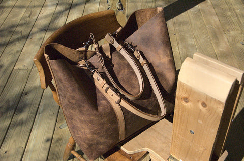 Wanderer Bag in rustic chair with straps resting down across the bag. Antique Copper clips and hardware and oiled leather handles. 