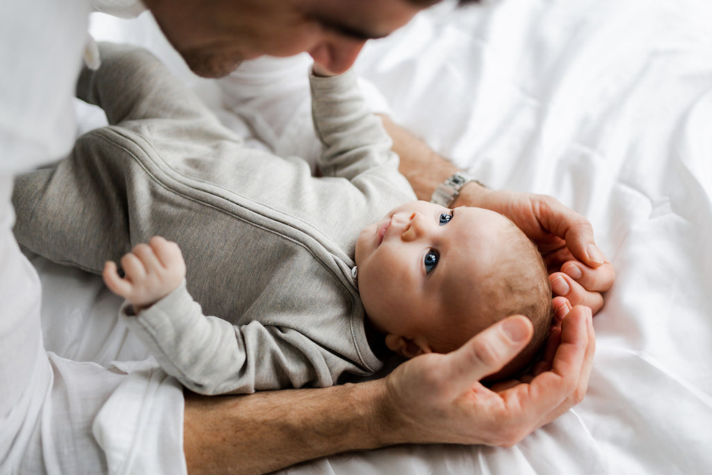 Dad looks at baby girl who wears plain onesie with zip made from organic pima cotton