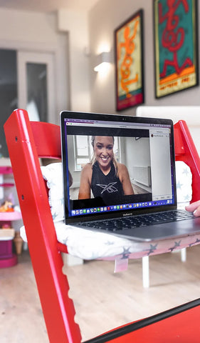 Laptop balanced on chair in lady's living room, showing exercise programme video