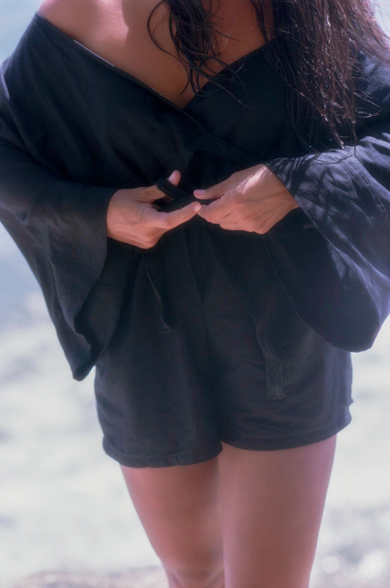 Body shot of model wearing black linen jumpsuit with kimono sleeves at beach