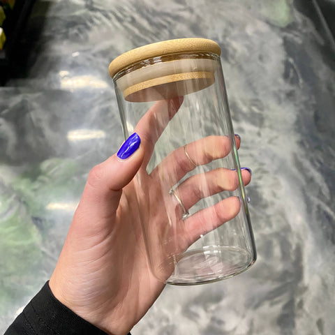 A white girl's hand with cobalt blue nails holds a large clear glass jar over a swirly gray floor.