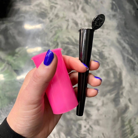 A white girl's hand with cobalt blue nails holds a small pink pop top vial and a black cone tube with the lid open.