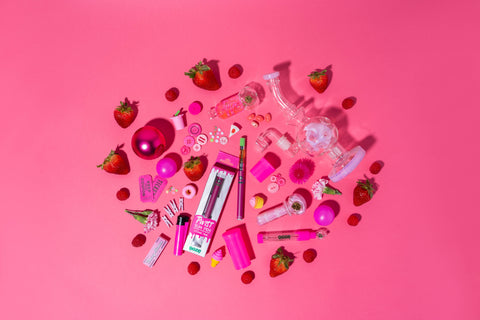 An overhead shot of a collage of different pink objects with an OozeX Strawberry Haze cartridge attached to a pink Ooze Slim Twist, strawberries, and other pink items on a pink background.