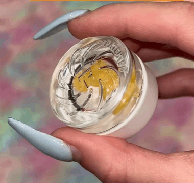 A girl with long light blue acrylic nails is holding an OozeX concentrate jar upside down to show the spinner carb cap grooves.
