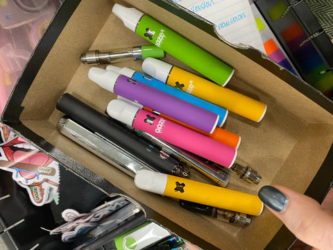 Empty OozeX disposable vapes, empty 510 oil cartridges, and old vape pen batteries are collected in a box in a drawer.