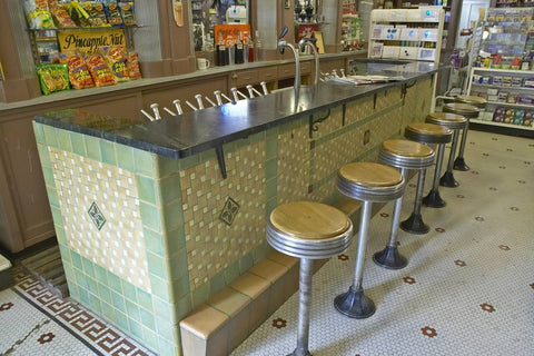 A counter with bar stools in a general store with a soda fountain.