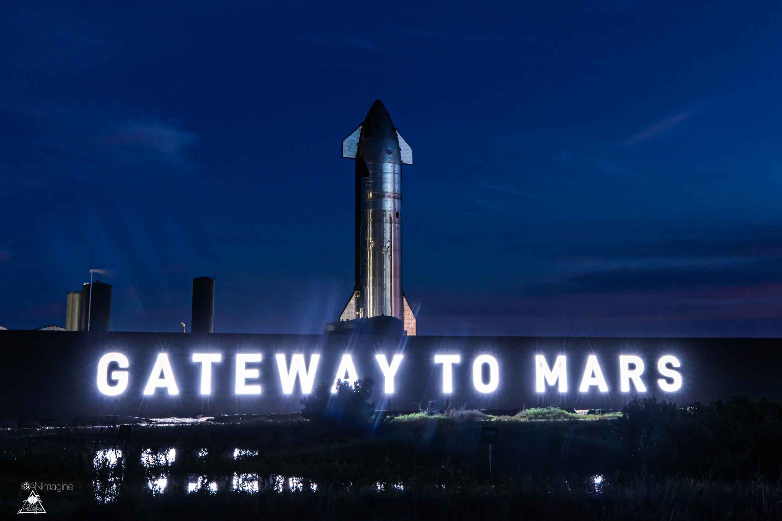 A Starship upper stage sits behind the illuminated "Gateway to Mars" neon sign at the Starbase launch site.