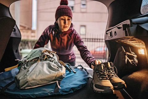 Eine Frau packt Wanderutensilien in den Kofferraum ihres Autos.