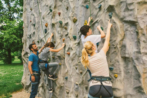 Ein Mann und eine Frau helfen zwei Kindern beim Klettern an einer Kletterwand.