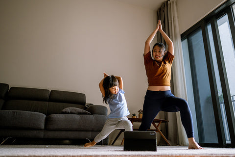 Eine Mutter und ihr Kleinkind machen in einem Wohnzimmer gemeinsam Yoga.