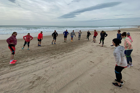 Eine Gruppe macht Sport an einem Strand, das Meer im Hintergrund.