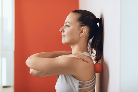 Eine Frau entspannt sich mit einem Massageball, während sie sich an eine Wand lehnt.