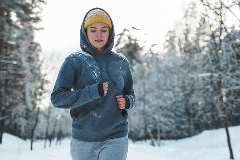 Eine Frau joggt in winterlicher Sportkleidung durch den Schnee.